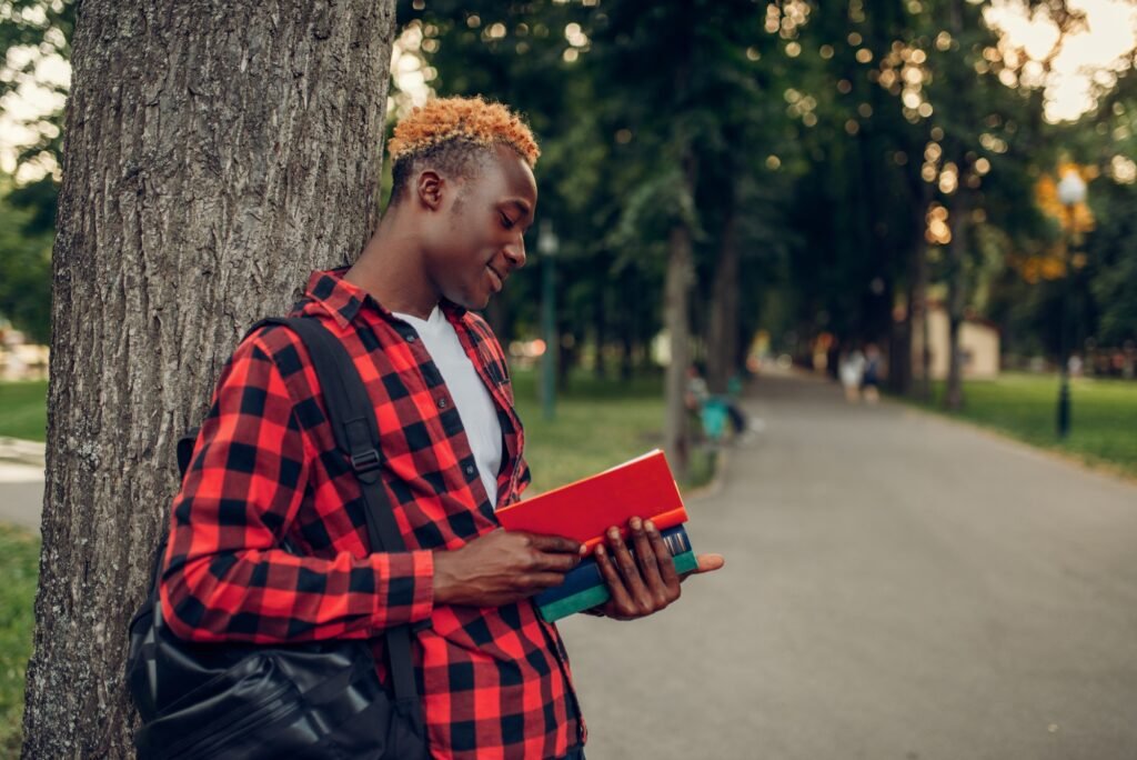 Black student with book and backpack in park